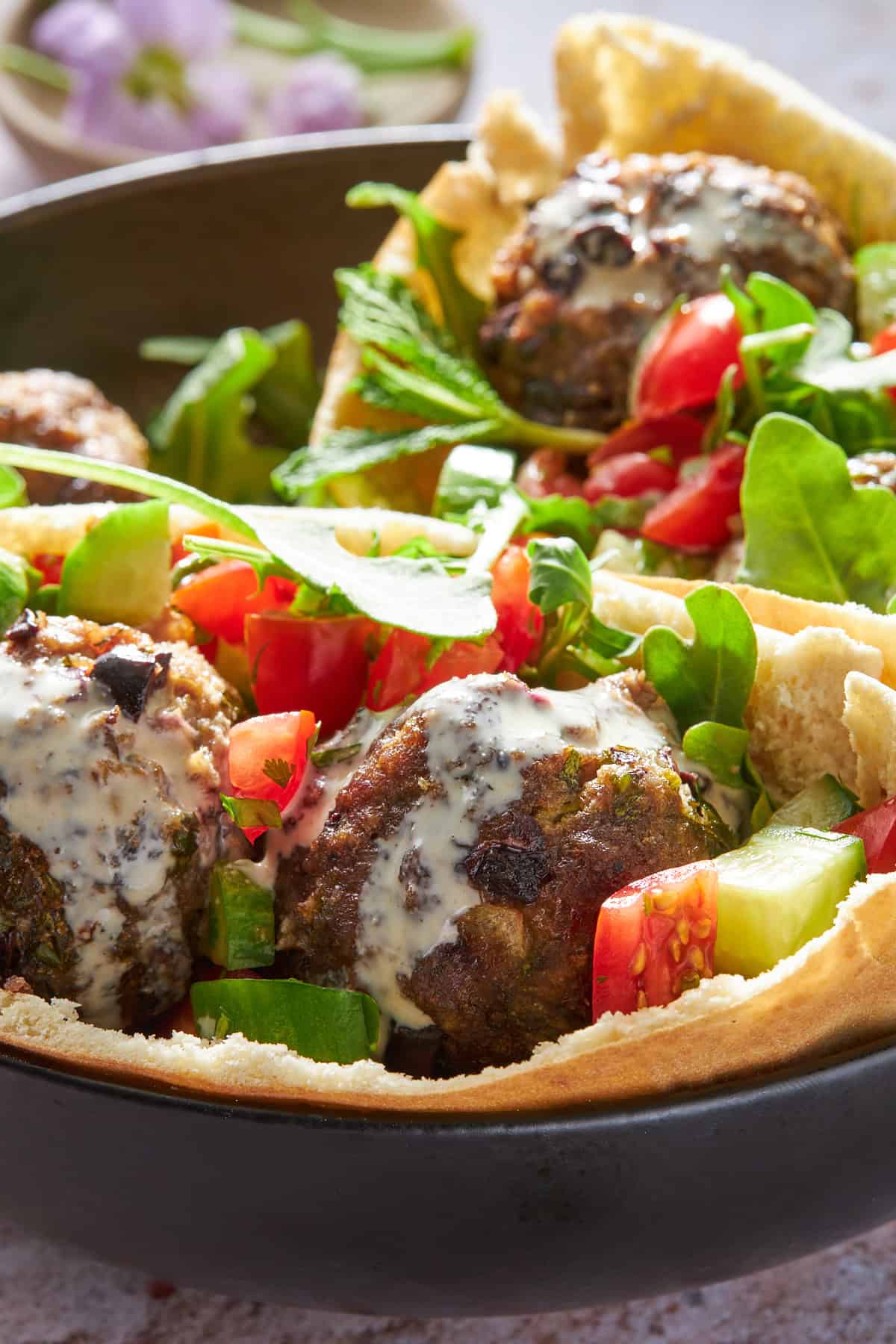 Two pitas with beef meatballs, tomato and cucumber salad, and tahini sauce.