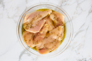Chicken breasts in a bowl with an olive oil marinade.