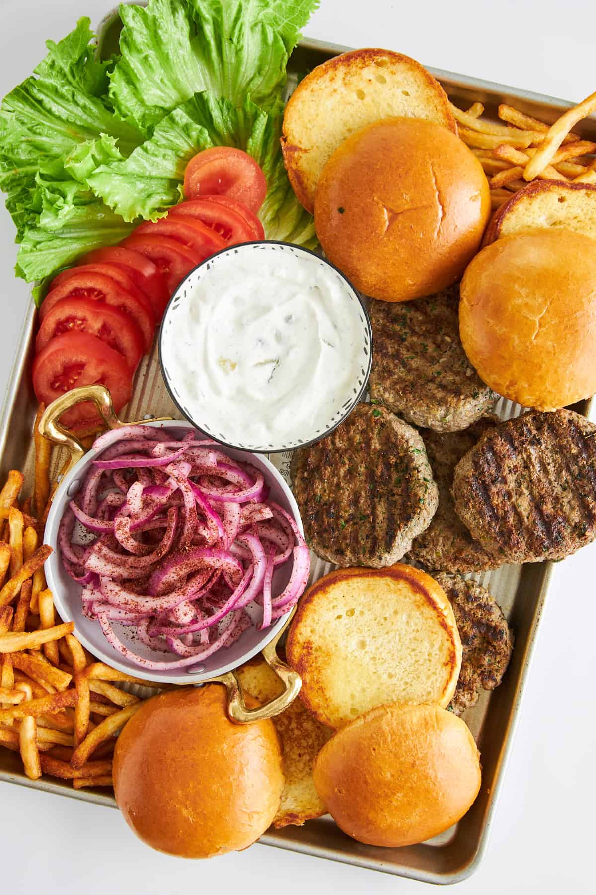 A platter of lamb kofta burger patties, buns, sumac onions, tomatoes, lettuce, and fries. 