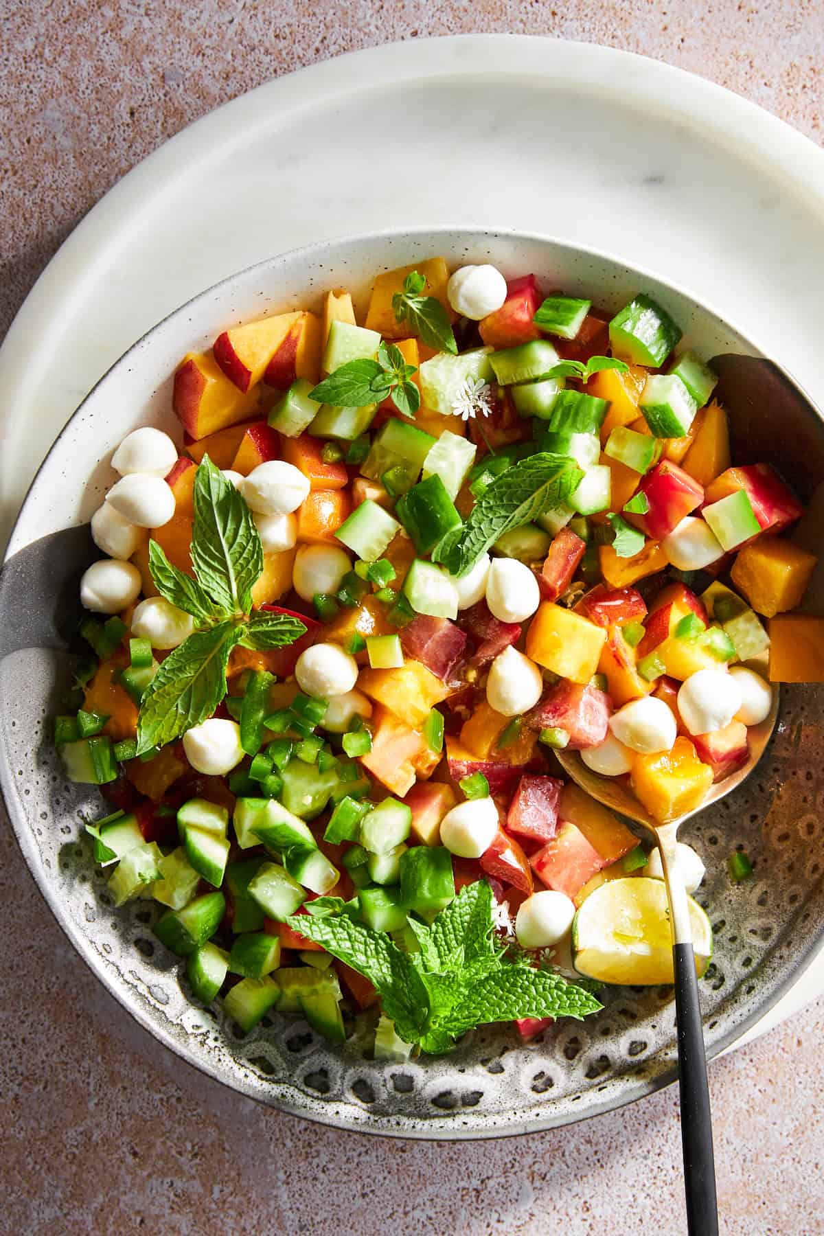 A bowl of peach salad with mozzarella pearls.