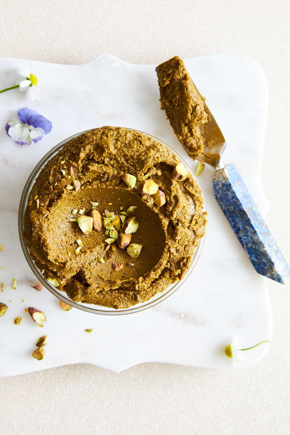 A jar of pistachio butter with a knife next to it. 