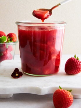 A spoon lifting a scoop of strawberry sauce from a jar.