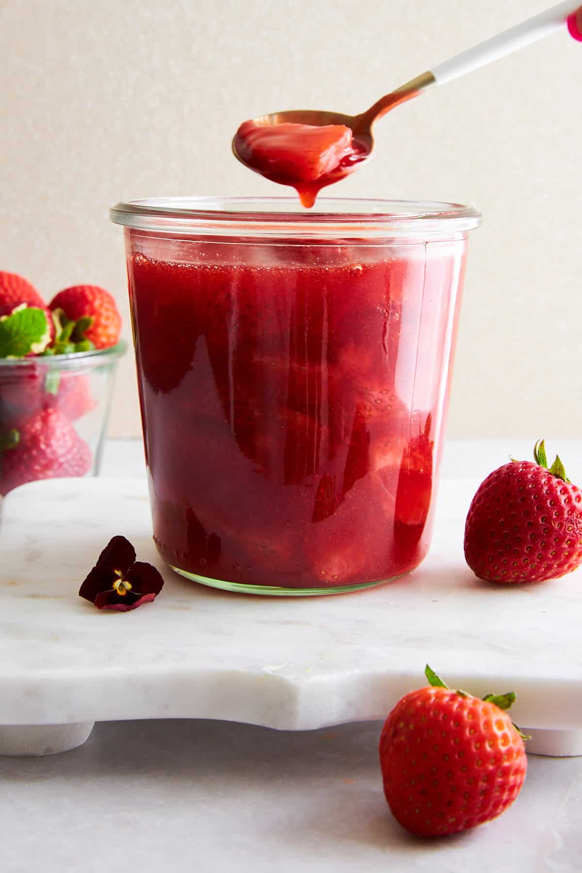 A spoon lifting a scoop of strawberry sauce from a jar. 