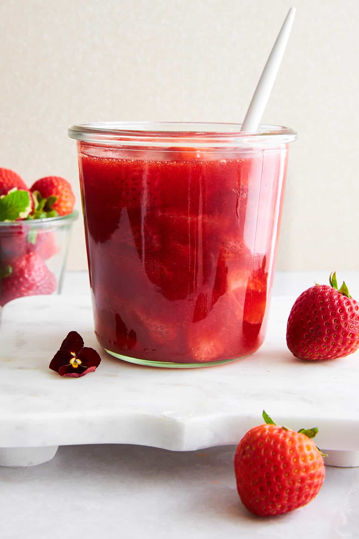 A jar of strawberry sauce with a spoon sticking out. 