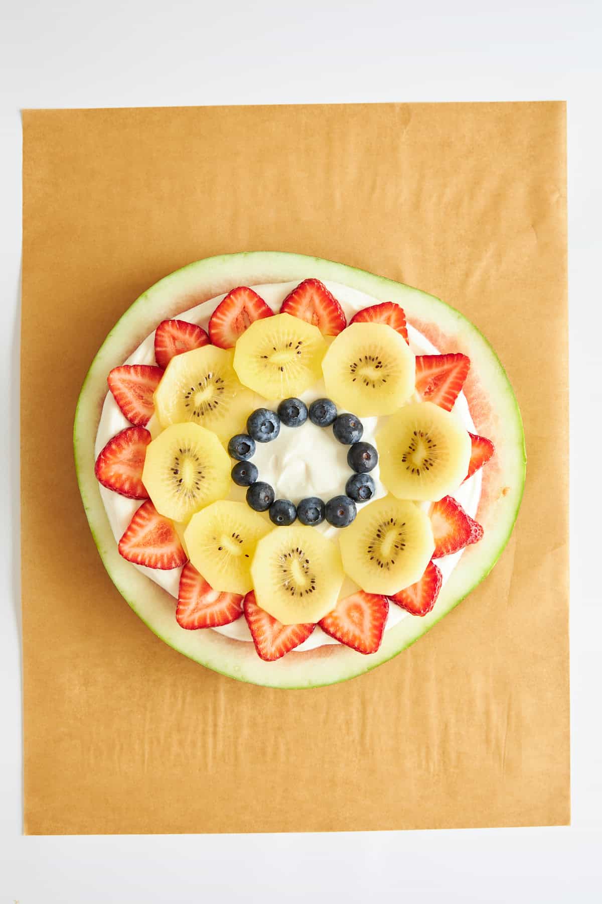 A watermelon round topped with yogurt, strawberries, kiwi, and blueberries.