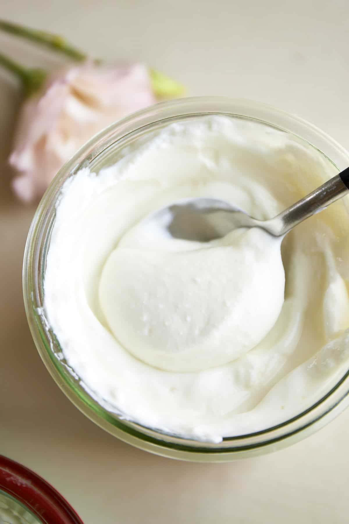 A spoon lifting a scoop of homemade Greek yogurt from a glass jar.