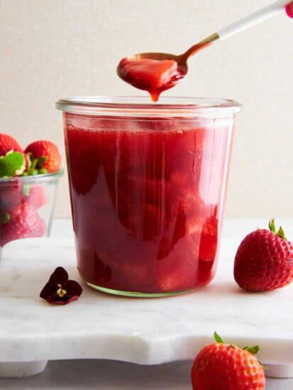 A spoon lifting a scoop of strawberry sauce from a jar.