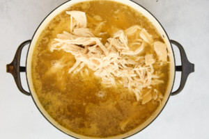 Shredded chicken floating in a pot of chicken noodle soup.