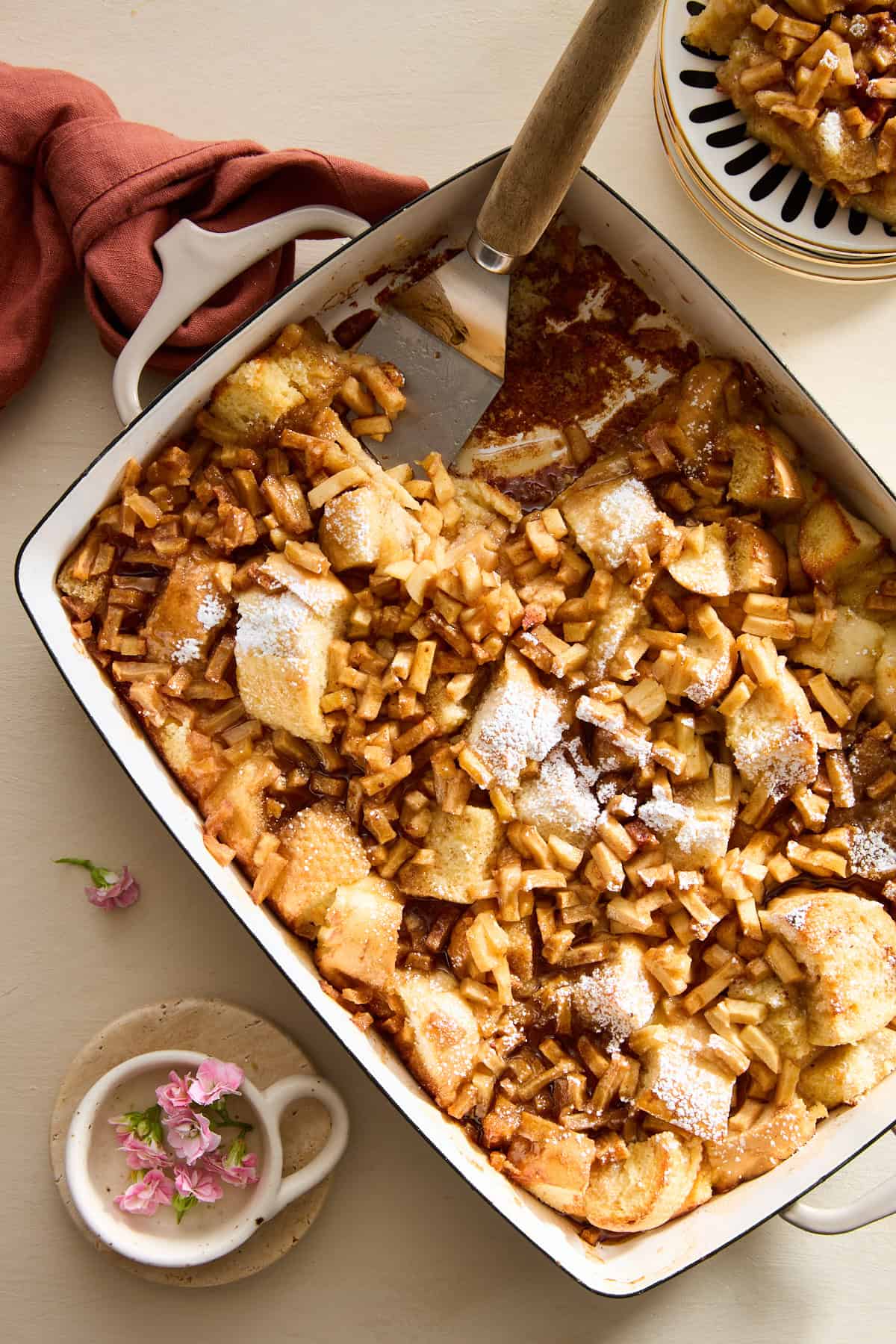 A serving dish of apple cinnamon french toast with a spatula in the spot of a missing serving. 