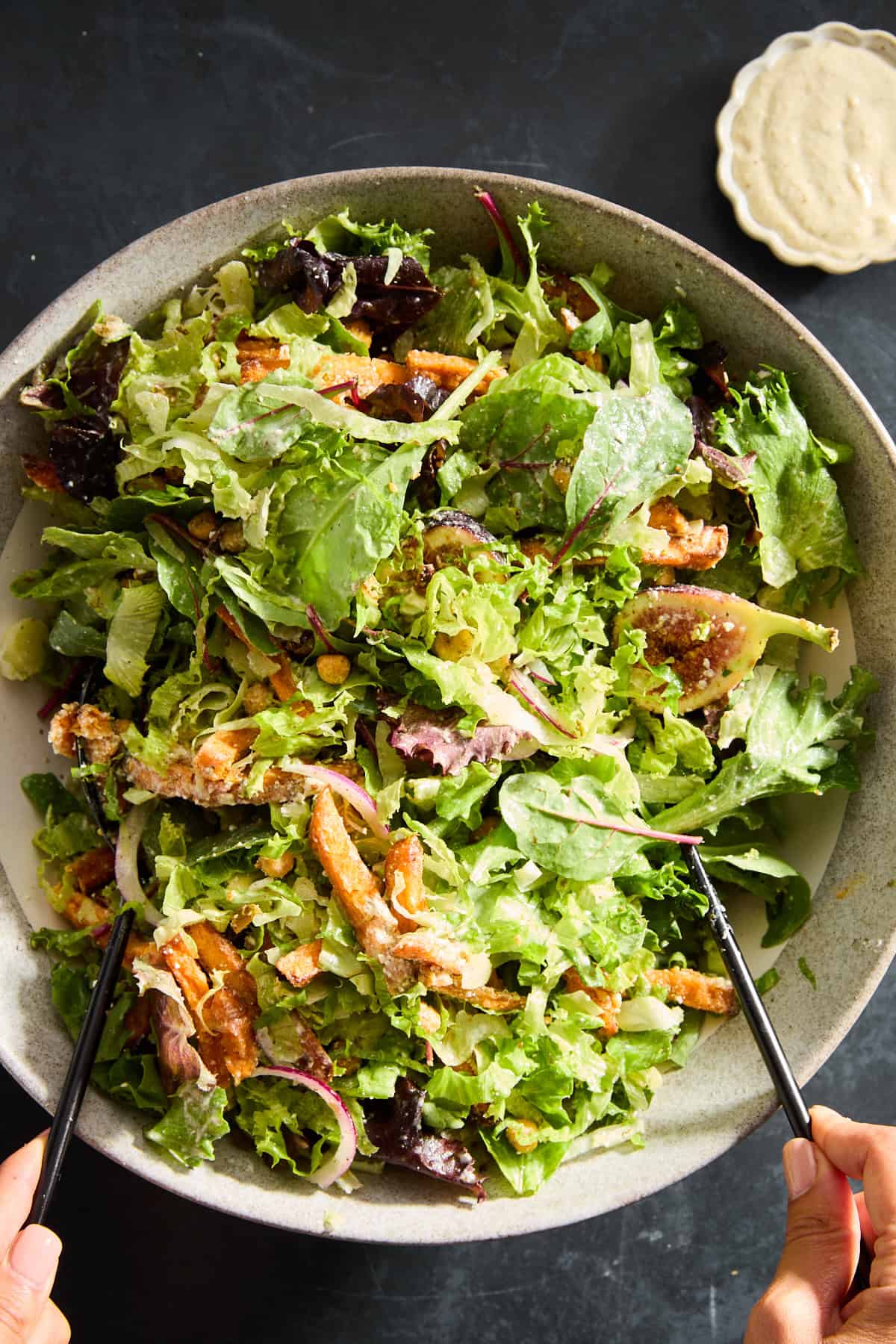 Two hands tossing a bowl of Roasted Carrots Chickpea Fig Salad. 