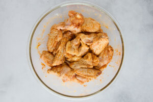 Raw chicken wings in a bowl tossed with seasonings.