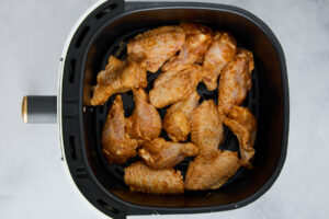 Raw chicken wings in an air fryer basket.