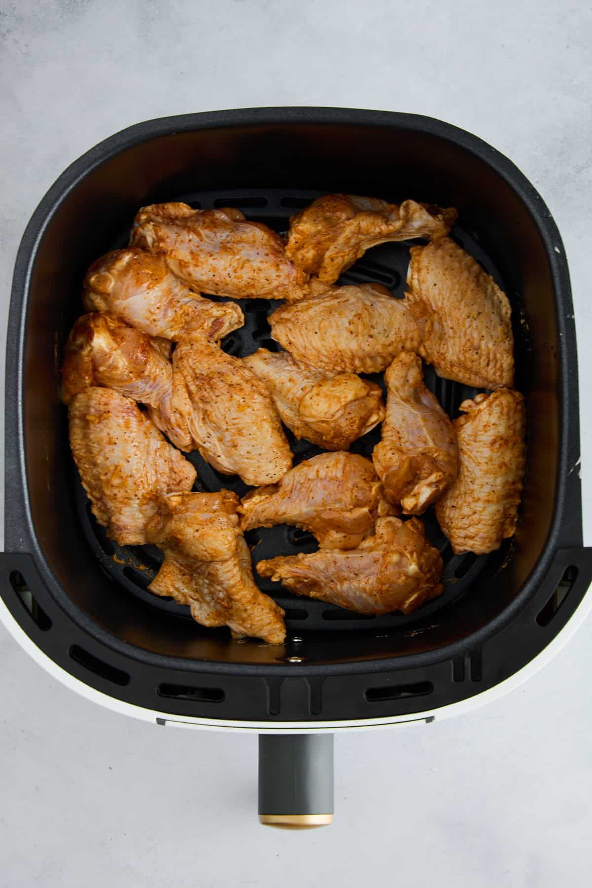 Raw seasoned chicken wings in an air fryer basket. 