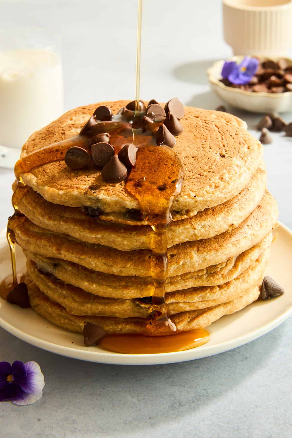 A stack of protein chocolate chip pancakes topped with chocolate chips and syrup. 