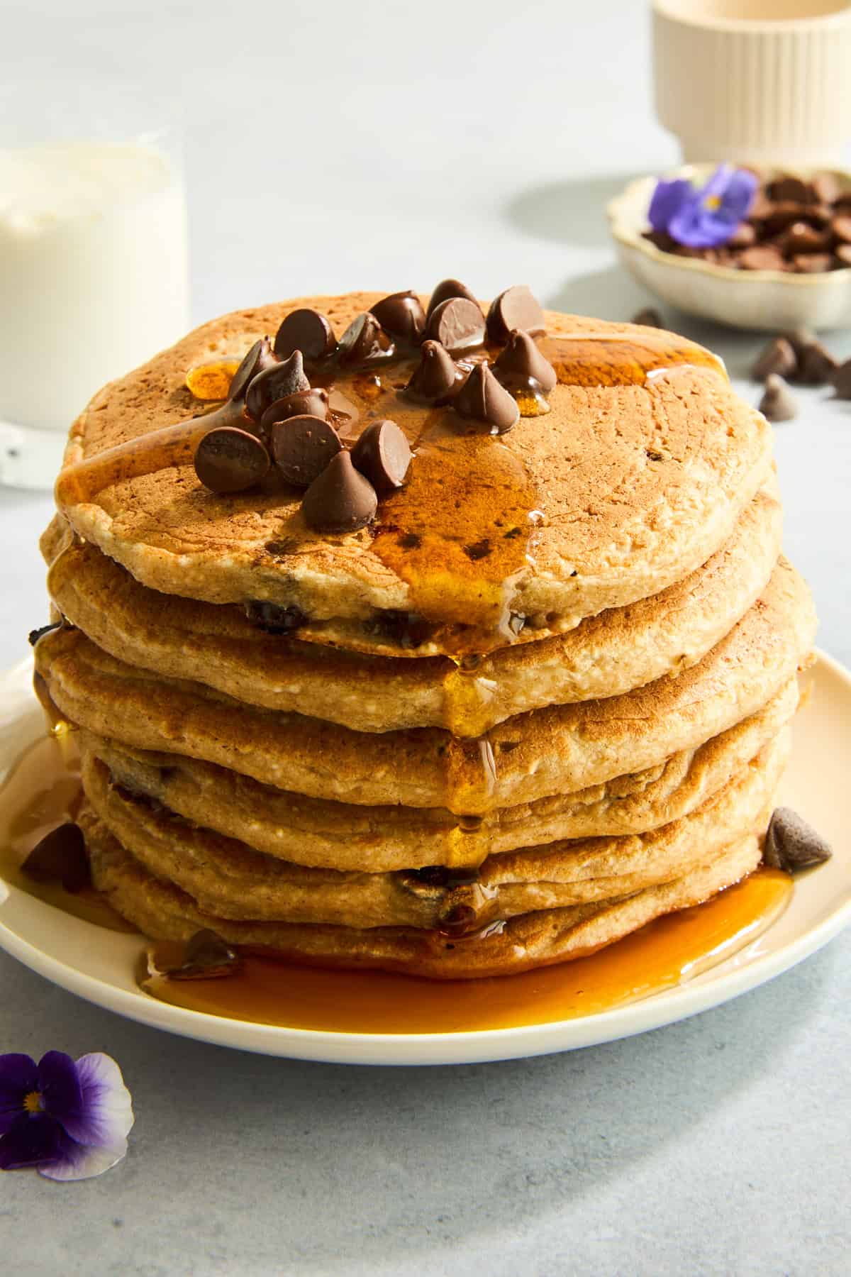 A stack of protein chocolate chip pancakes topped with chocolate chips and syrup. 