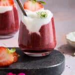 A jar of strawberry chia pudding topped with yogurt and a strawberry.