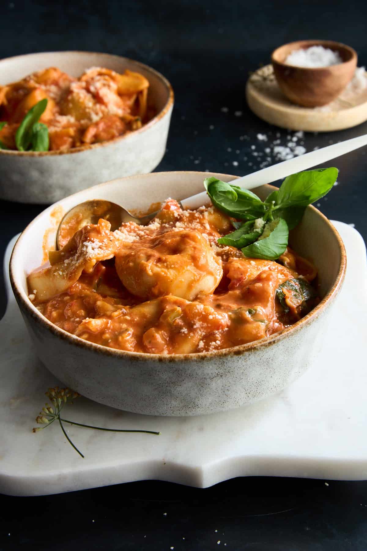 A bowl of cheese tortellini soup with a spoon sticking out. 