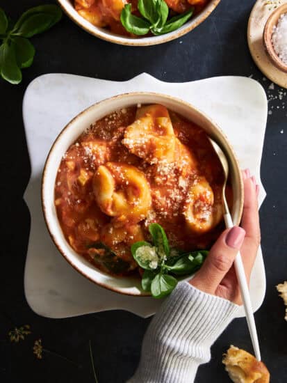 A hand wrapped around a bowl of cheese tortellini soup.