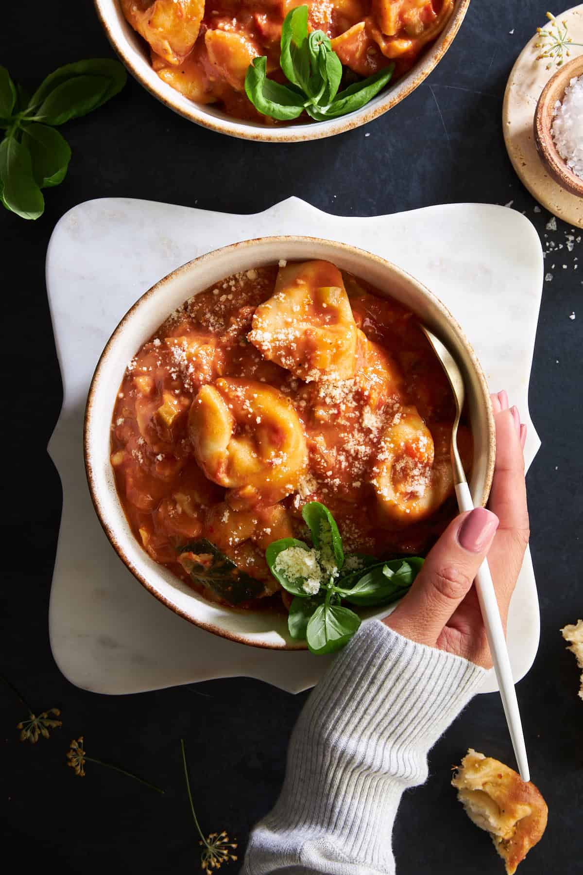 A hand wrapped around a bowl of cheese tortellini soup.