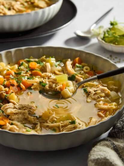 A spoon lifting a bite of chicken noodle soup from a bowl.