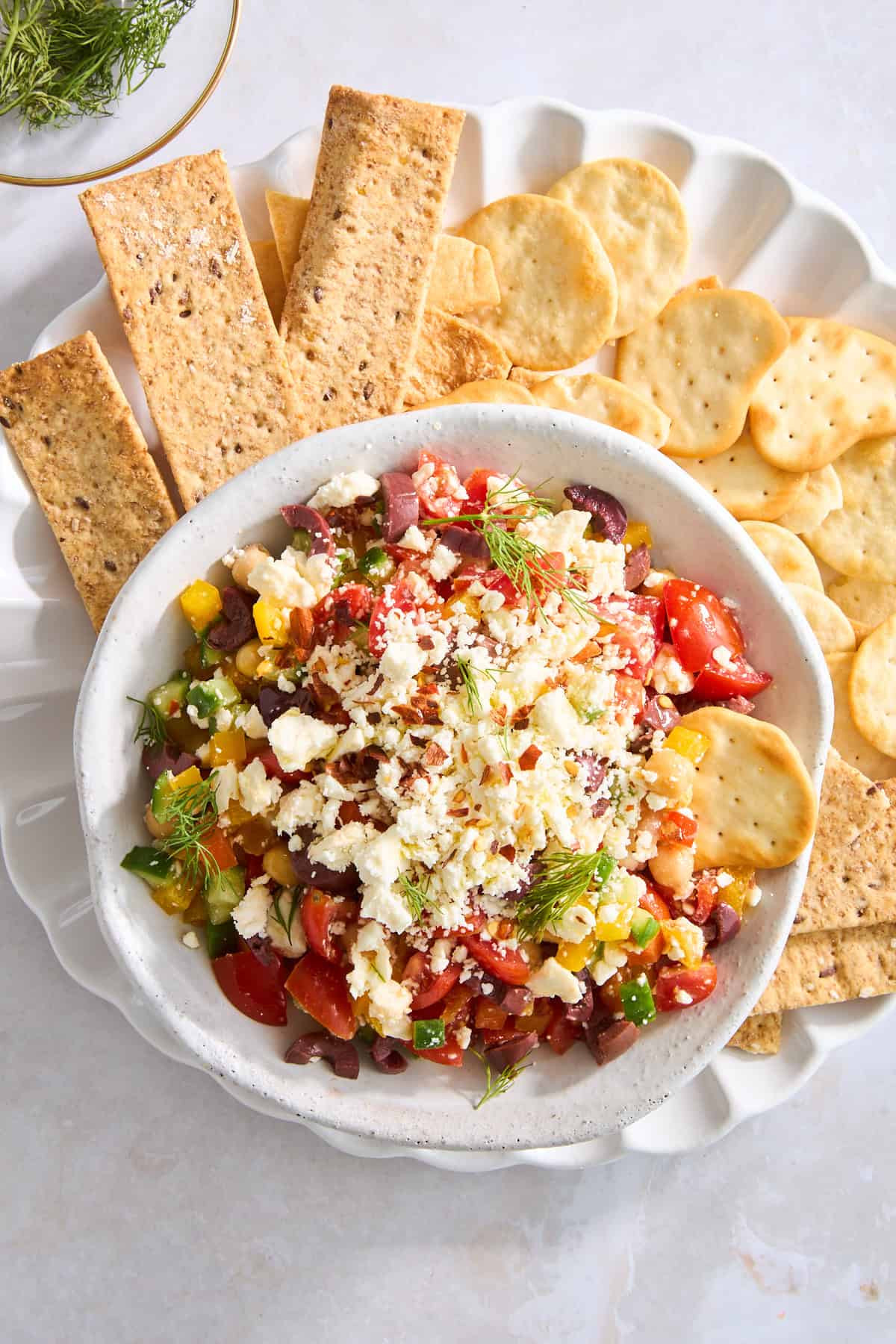 A bowl of Mediterranean feta dip on a plate with pita chips and crackers. 