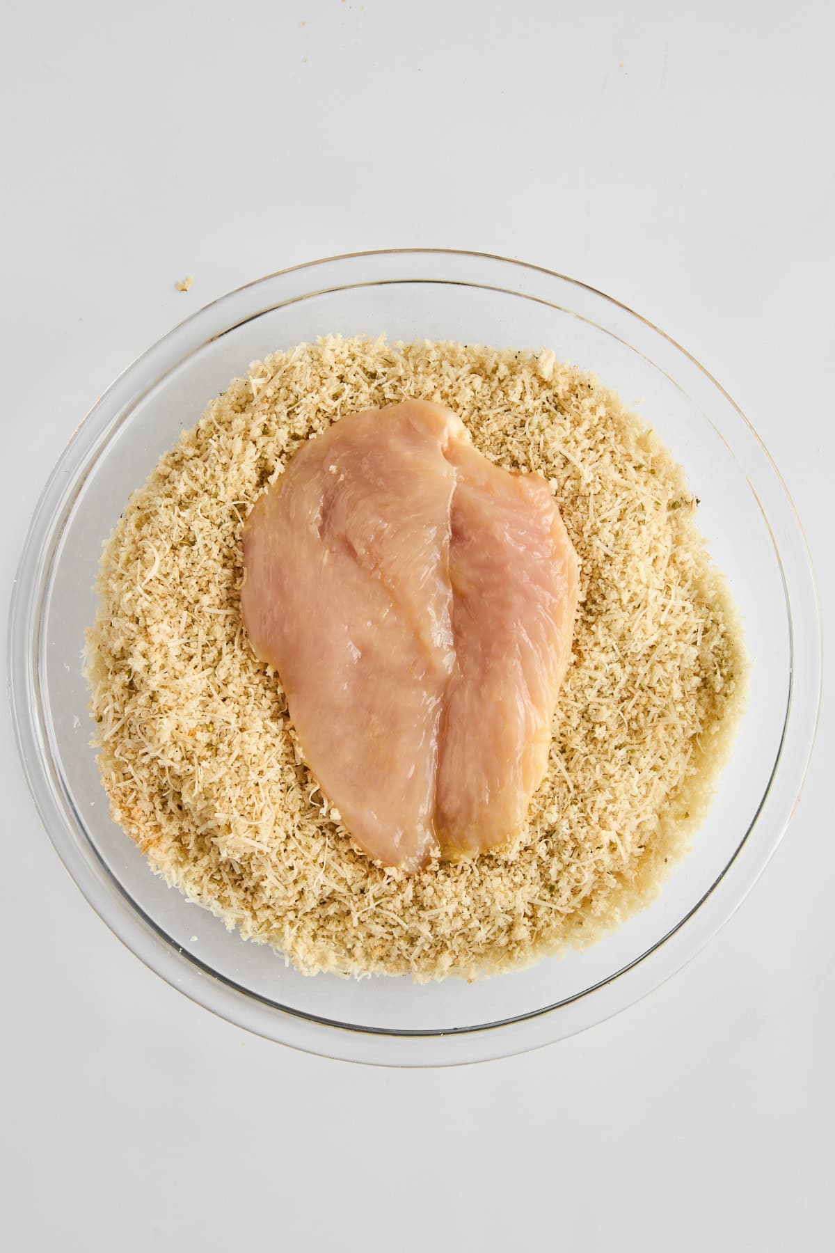 Raw chicken pieces being dredged in breading. 