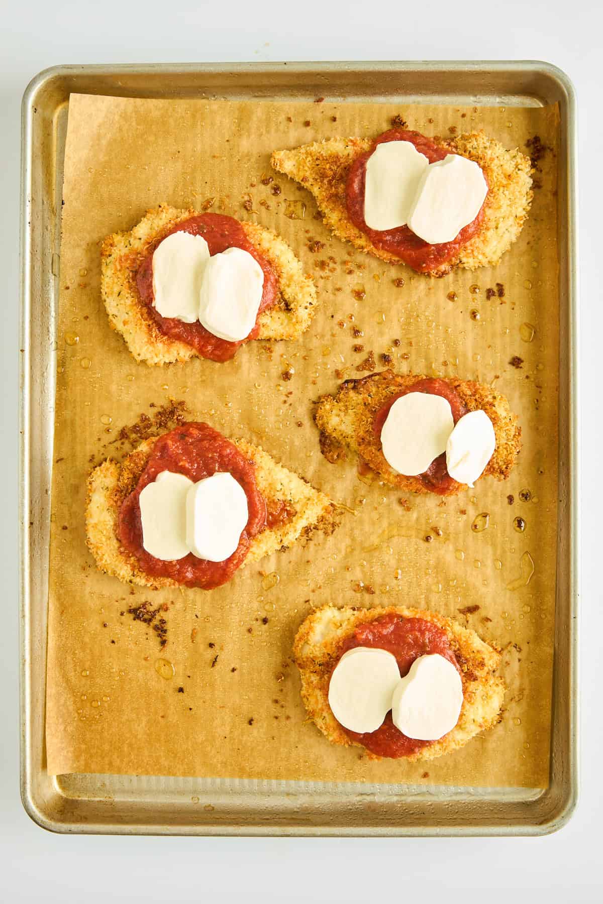 Unbaked chicken parmesan on a baking sheet. 