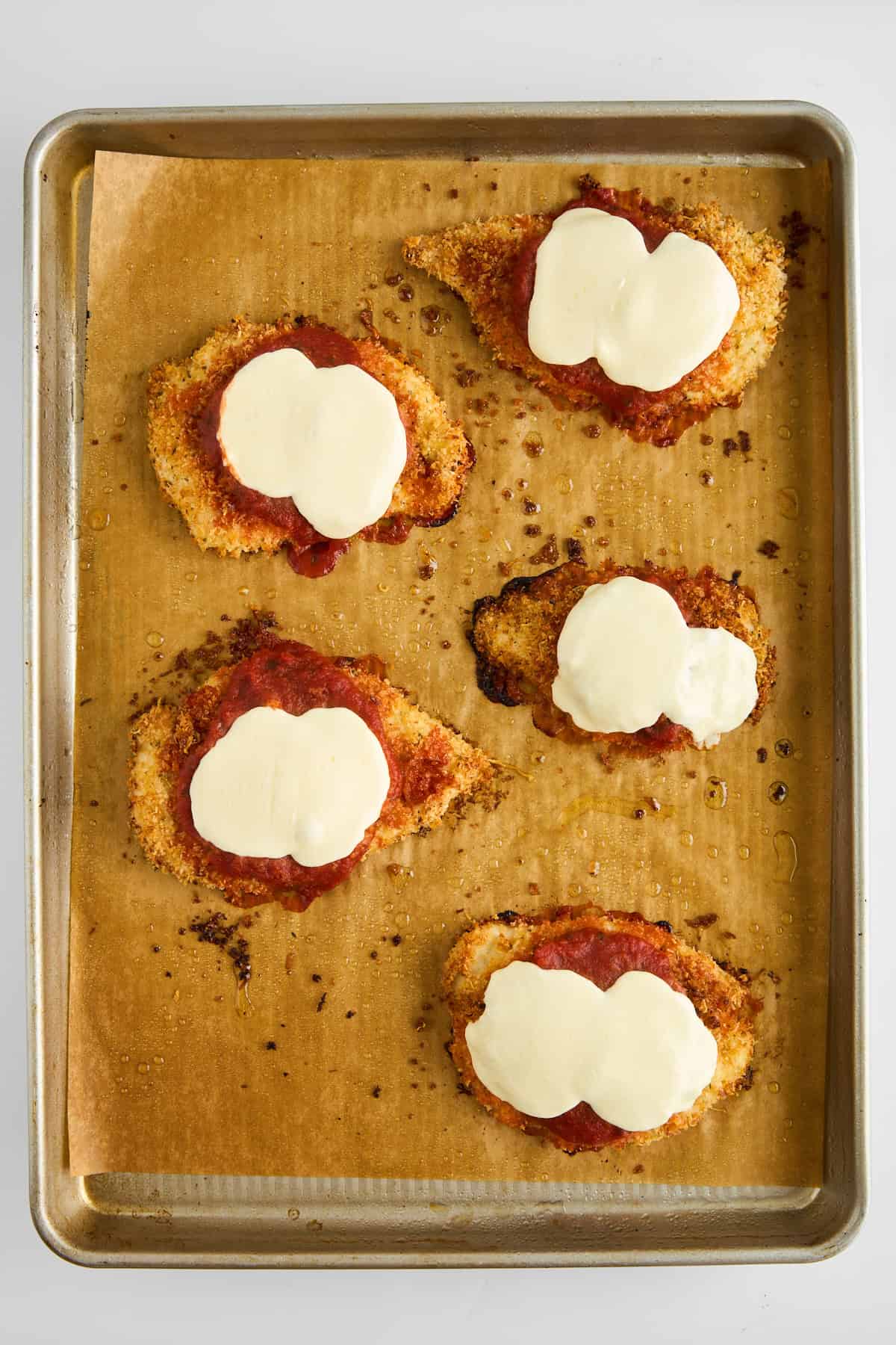 Five baked chicken parmesan pieces on a baking sheet. 