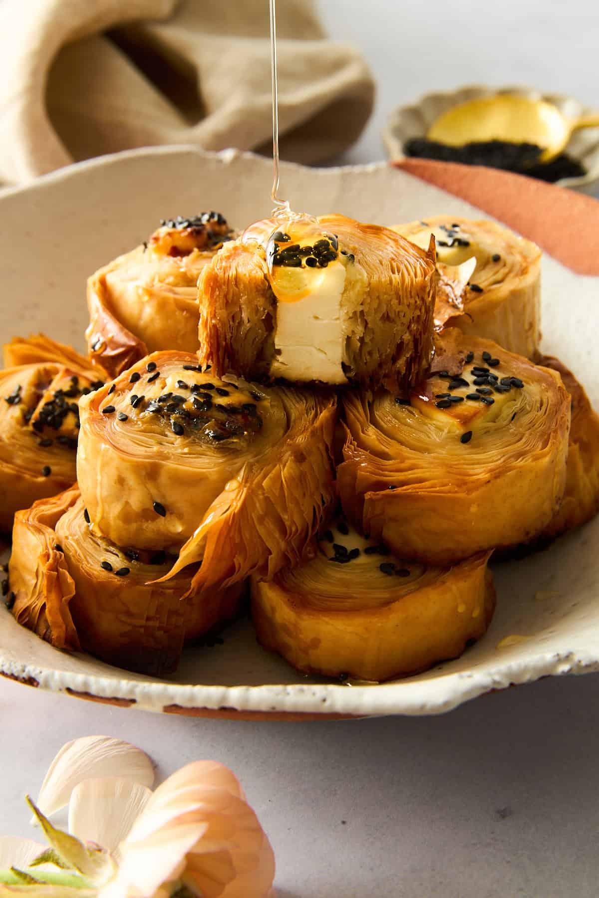 A plate of hot honey phyllo rolls with honey being drizzled on top. 