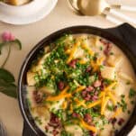 A bowl of cheesy potato soup topped with bacon, chives, and cheese.