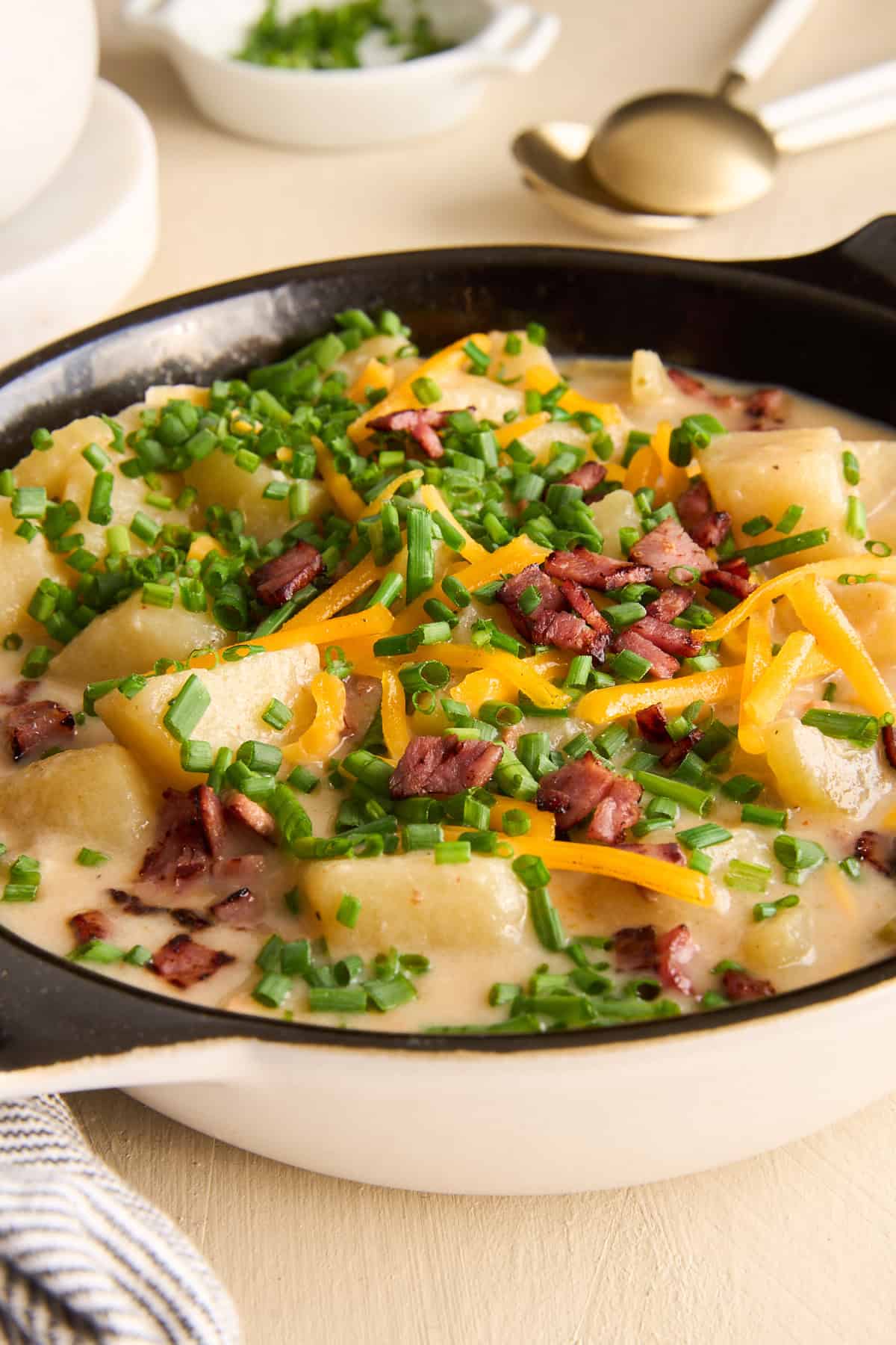 Close up side view of a bowl of cheesy potato soup topped with chives, cheese, and bacon.