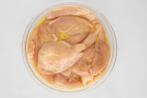 Raw chicken being dredged in egg wash.