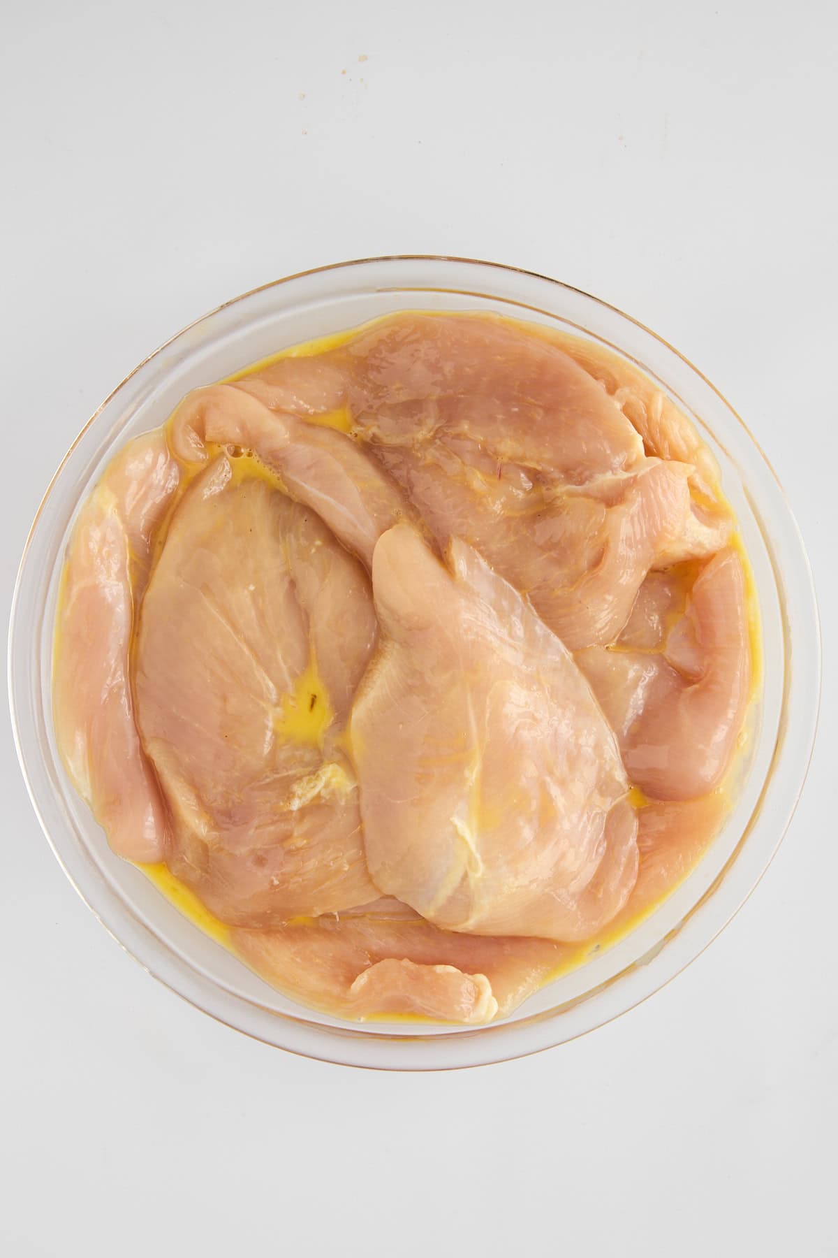 Raw chicken being coated in egg wash. 