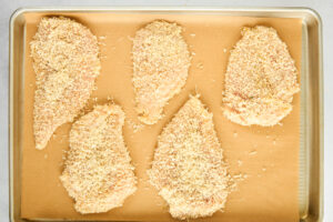 Breaded chicken pieces on a parchment paper lined baking sheet.