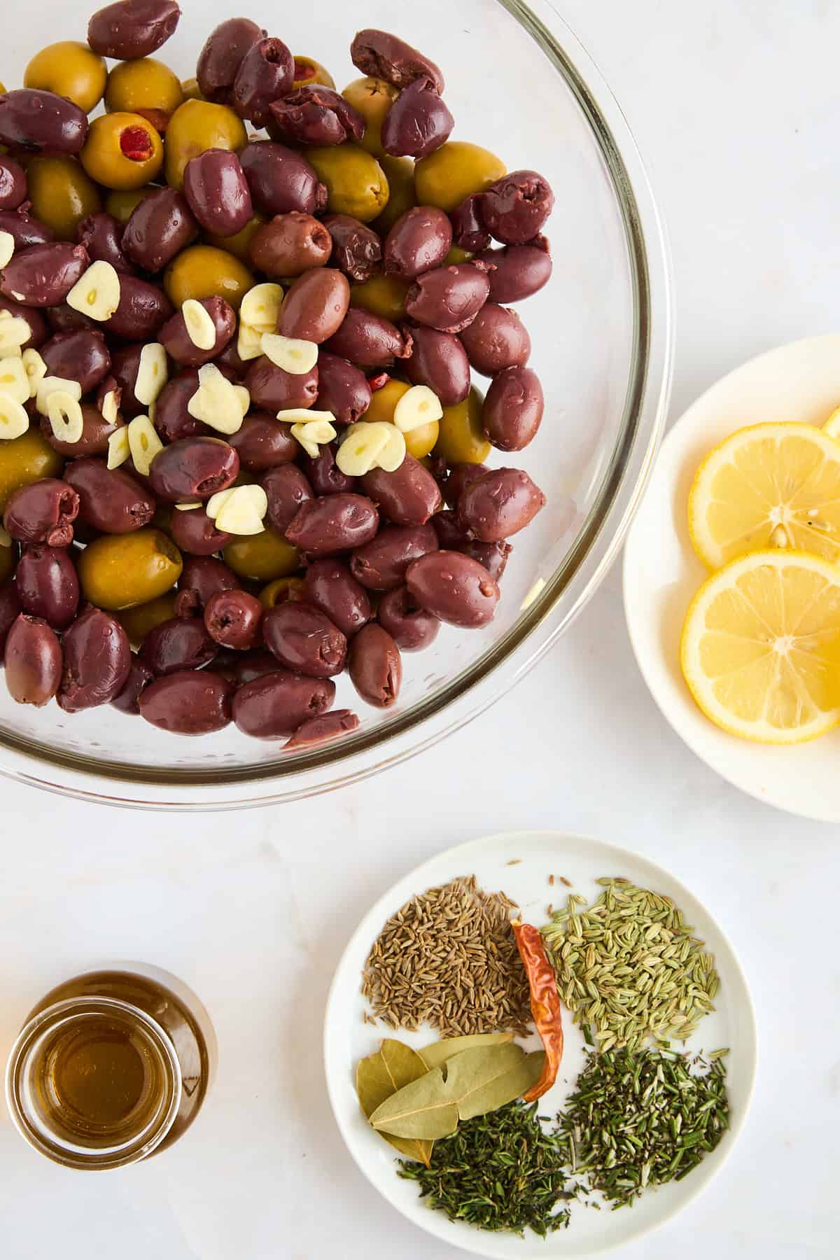 A bowl of olives, seasonings, lemons, and olive oil. 