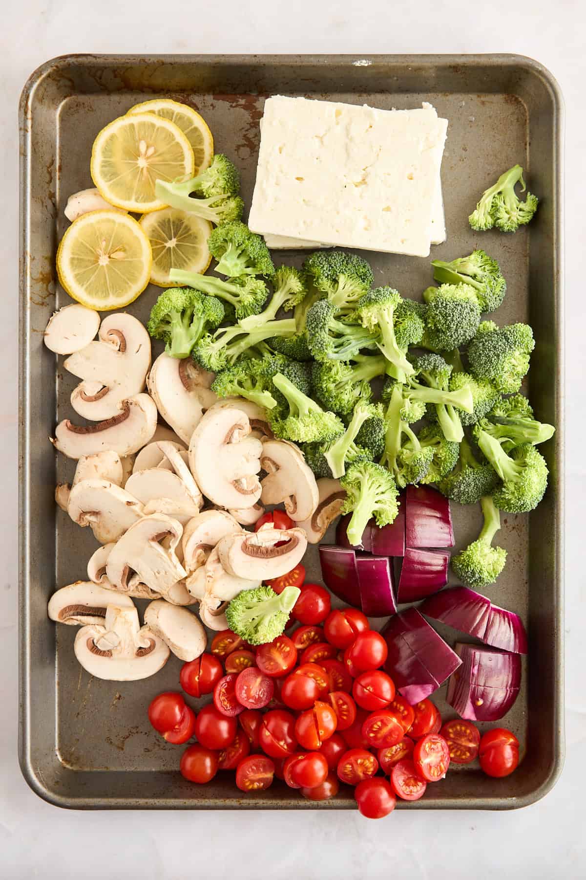 Raw veggies and feta blocks on a sheet pan. 