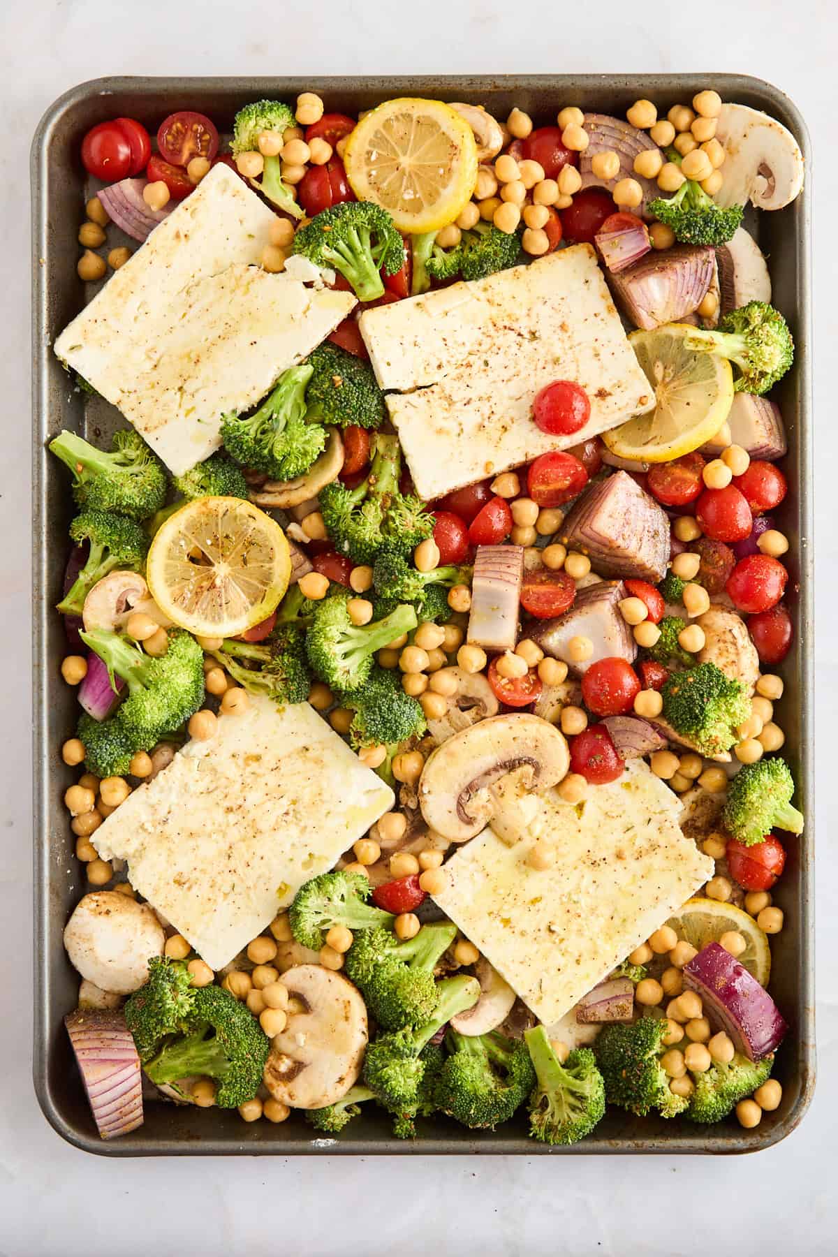 Seasoned raw veggies, feta, and chickpeas on a sheet pan. 