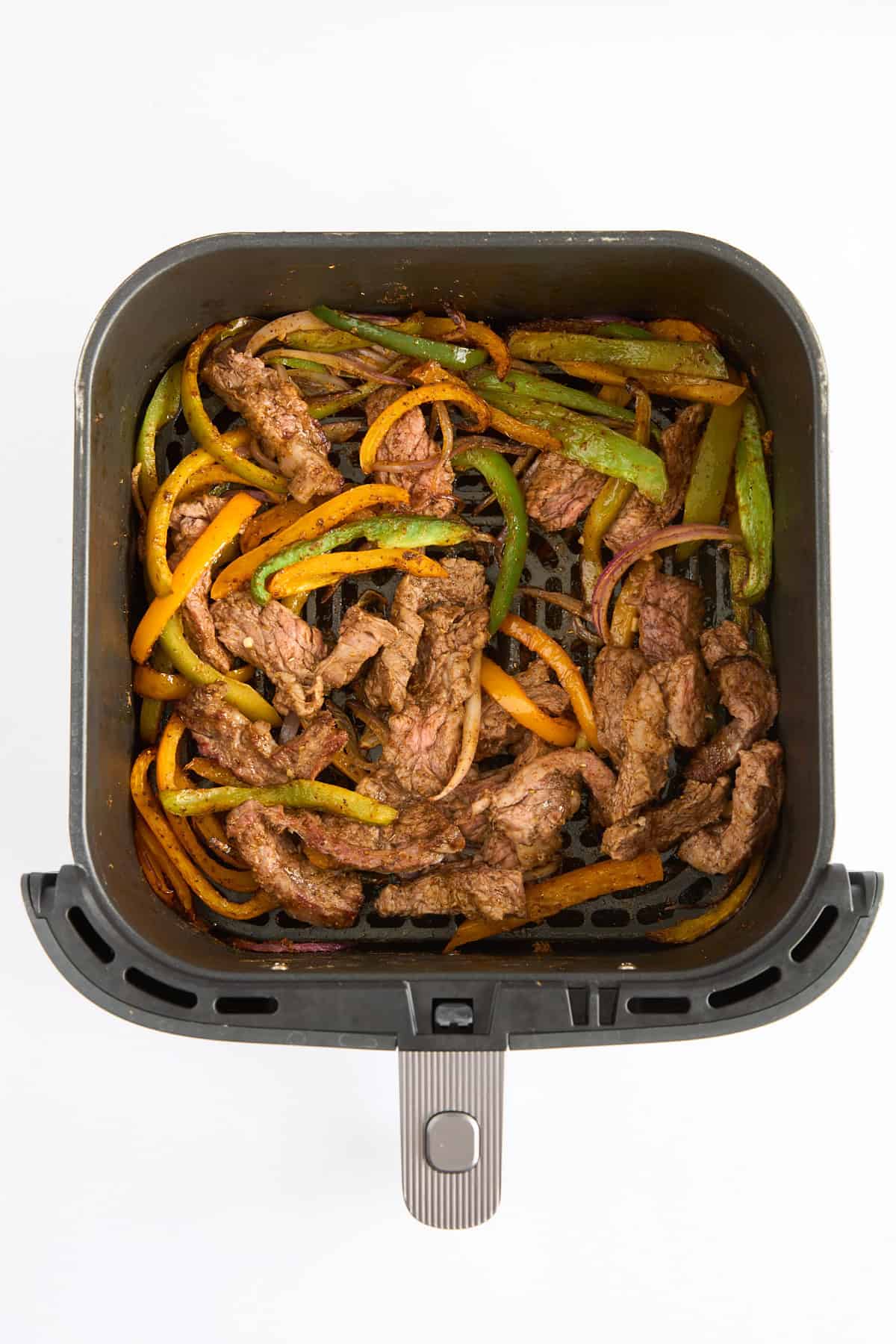 Cooked steak fajitas in an air fryer basket. 