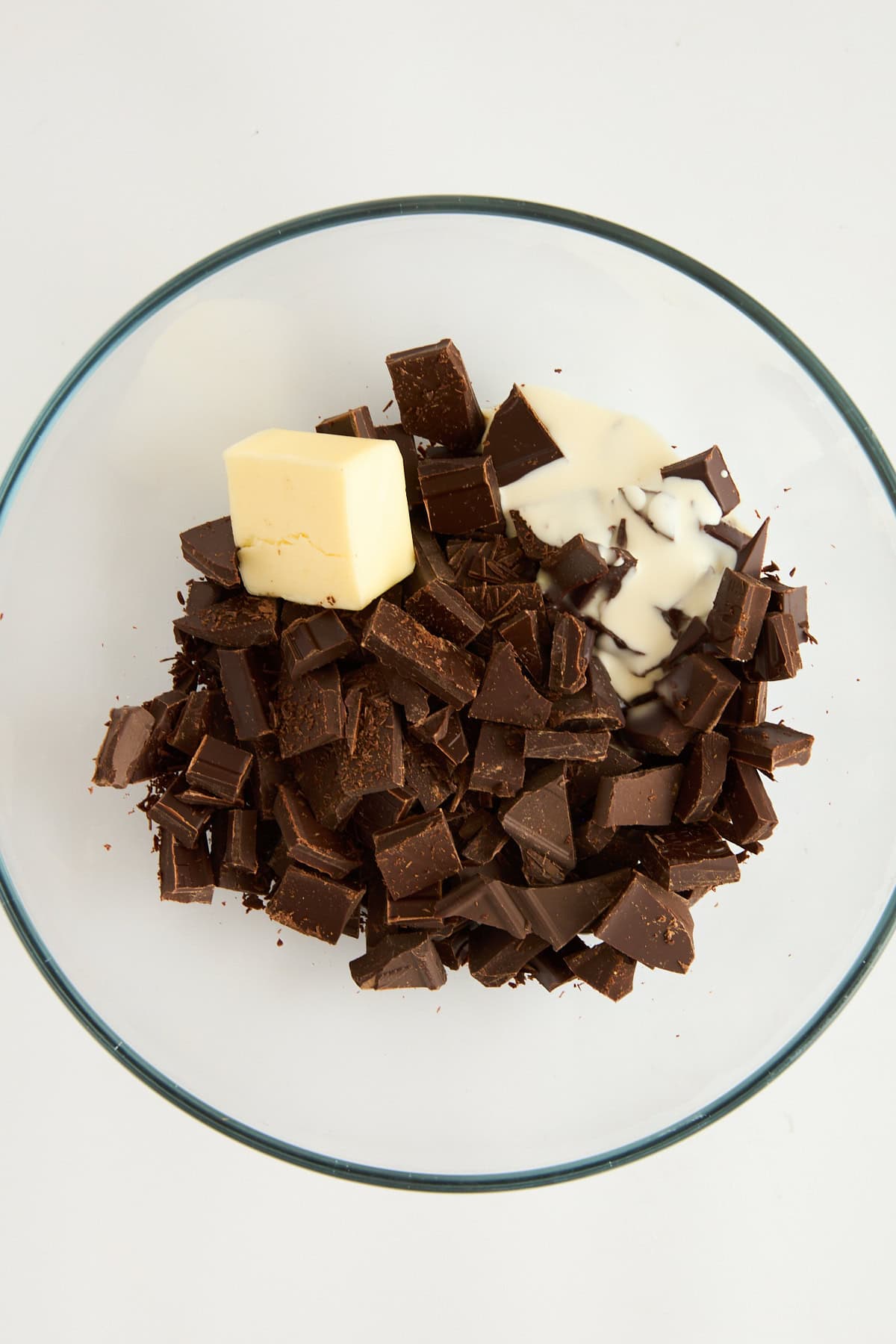 Chopped chocolate, butter, and heavy cream in a bowl. 