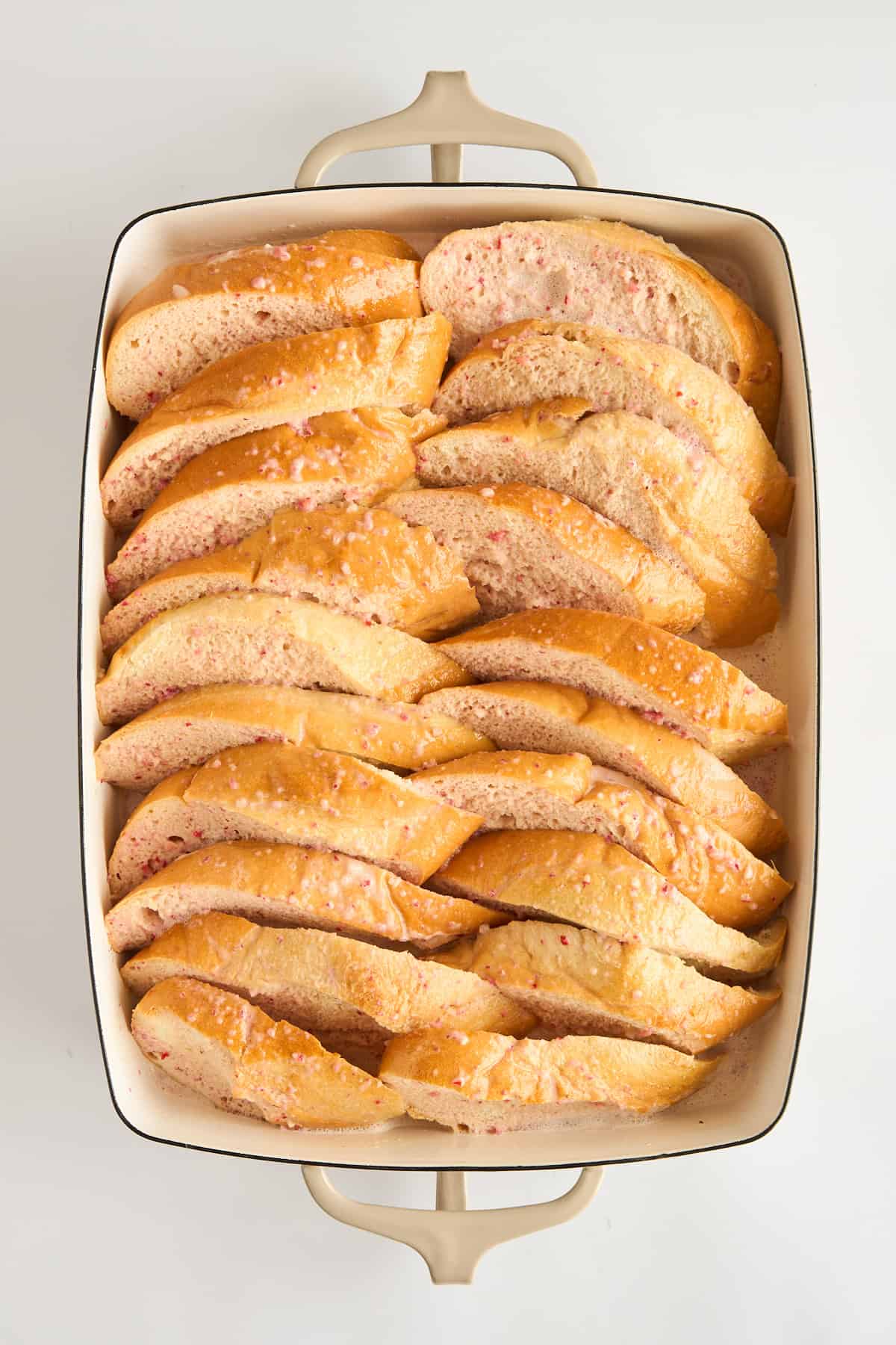 Bread pieces in a baking dish coated in a strawberry custard. 