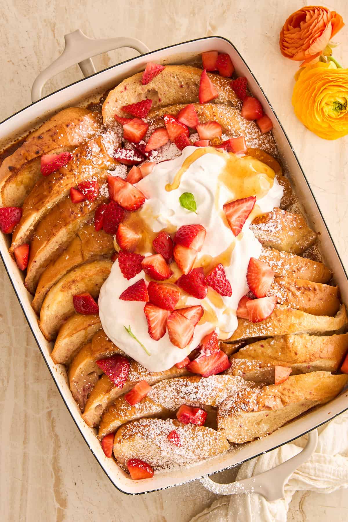 A baking dish of strawberry french toast topped with whipped cream and strawberries.