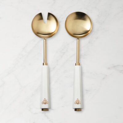 A set of two golden salad servers on a marble surface.