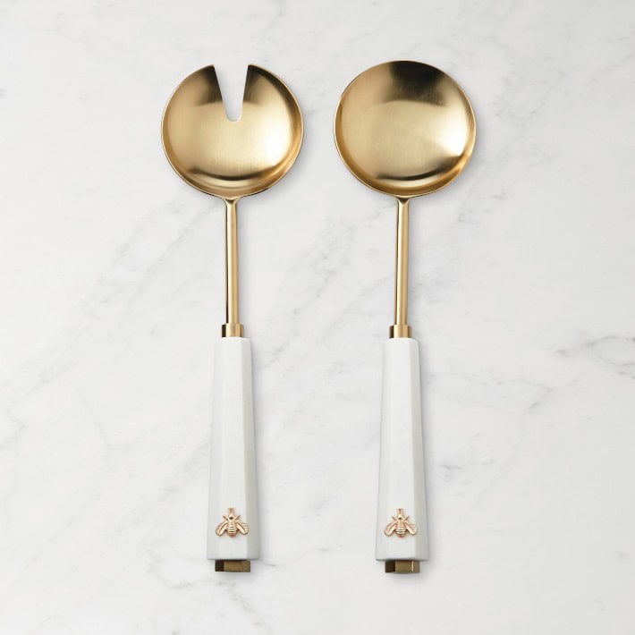 A set of two golden salad servers on a marble surface. 